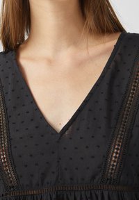 Top in tessuto nero con scollo a V, caratterizzato da punti testurizzati e bordo in pizzo lungo lo scollo e le maniche, creando un effetto stratificato.