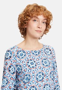Bluse mit floralem Muster in hellblau, dunkelblau und Koralle. Weicher Stoff mit rundem Ausschnitt und langen Ärmeln.