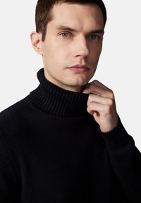 Czarny sweter z kołnierzem i mankietami ściągaczowymi, z teksturowanym wzorem dzianiny. Model trzyma kołnierz na neutralnym tle.