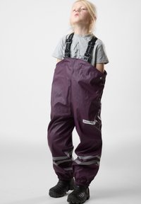 Purple waterproof overalls with adjustable straps, reflective accents, and elastic cuffs, paired with black boots. Smooth, durable material.