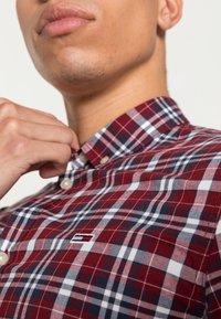 Röd och marinblå rutiga skjorta med knapp-ner krage, som har vita detaljer och en liten broderad logotyp på bröstet.