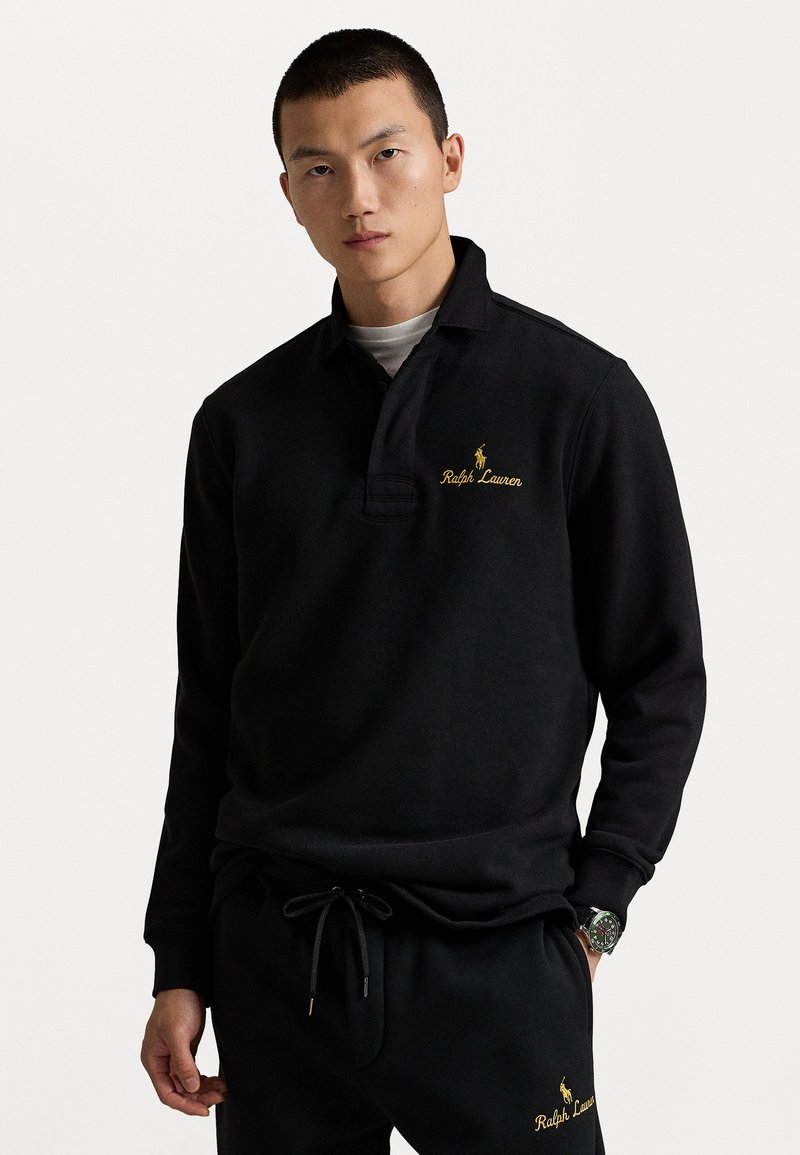 Melns garo piedurknu pola krekls, izgatavots no kokvilnas, ar apkakli, kas rotāta ar izšūtu dzelteno "Ralph Lauren" logotipu un nelielu zirdziņa emblemu uz krūšu.