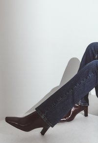 Talons aiguilles en cuir verni bordeaux avec un petit talon carré, assortis à un jean en denim bleu foncé avec un léger évasement en bas.