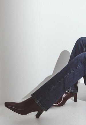 Decollete in vernice bordeaux a punta con tacco basso e blocco, abbinate a jeans in denim blu scuro con una leggera svasatura in fondo.
