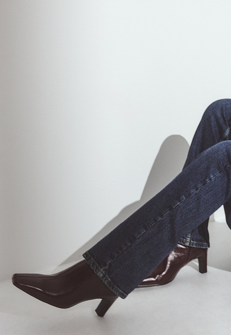 Talons aiguilles en cuir verni bordeaux avec un petit talon carré, assortis à un jean en denim bleu foncé avec un léger évasement en bas.
