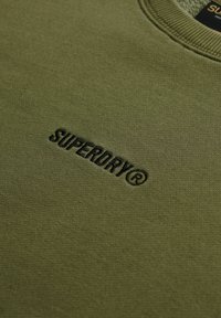 Groene sweatshirt van zacht materiaal, met een reliëf 'SUPERDRY®' logo in donkere draad aan de voorkant. Klassiek ronde hals ontwerp.
