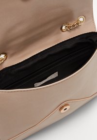 Beige kožená kabelka s černou textilní podšívkou, obsahující zipovou kapsu a zlaté kovové detaily.