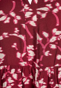 Rausvas suknelė su gėlių raštu, kuriame dominuoja rožinės ir smėlio spalvos. Suknelėje yra V formos iškirpė, surinkta talija, minkšta tekstūruota medžiaga ir matomi siuvimo detalės.