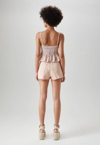 Smocked blomsterbluse med peplumkant, parret med lyserøde slidte shorts og beige platform sandaler. Baggrunden er neutral grå.