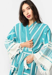 Tirkizni pamučni kimono s bijelim prugama, velikim rukavima i resastim rubovima. Ima pojas s remenom u struku i dva bočna džepa.