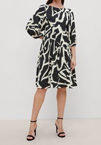 Robe à motifs noir et crème avec des manches bouffantes et une jupe évasée. Le tissu a une texture lisse et est décoré de lignes courbes et de points.