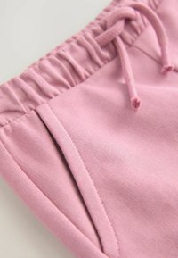 Ljust rosa bomullsjoggers med elastisk midja och snörning, har platta fickor och en mjuk textur.