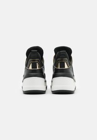 Schwarze und goldene Sneaker mit einem glatten Lederobermaterial, gepolstertem Kragen und weißer Zwischensohle mit markanten strukturierten Akzenten.