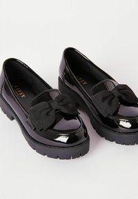 Czarne lakierowane mokasyny ze skórzanym, teksturowanym kokardą, wyposażone w grubą czarną gumową podeszwę oraz subtelne ząbkowane przeszycia.