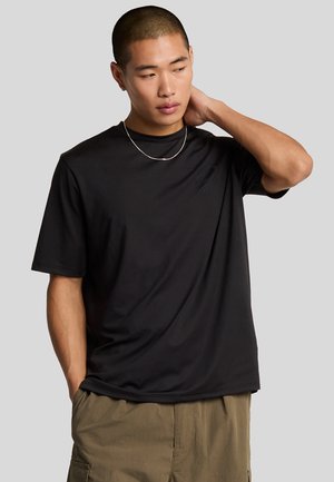 Svart kortärmad t-shirt i mjukt tyg, med en diskret logotyp på bröstet, tillsammans med olivgröna cargoshorts.