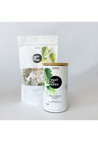 Witte cilindrische container met een bamboe deksel, gelabeld "Recharge Baby!" naast een witte zak met kruidenafbeeldingen en de tekst "I Want You Naked."