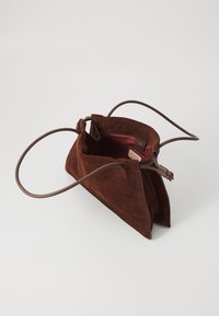 Geantă din piele de căprioară maro, cu o formă triangulară și o textură moale. Prezintă o curea maronie și un interior roz. Închidere cu fermoar în partea de sus.