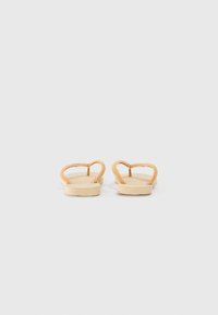 Infradito in suede marrone con suole piatte beige e un design minimalista, caratterizzate da una tracolla a forma di cuore per un tocco in più.