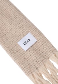 Ljusbeige scarf gjord av texturerat tyg, med fransade ändar och en vit etikett med "CECiL" tryckt i svart.