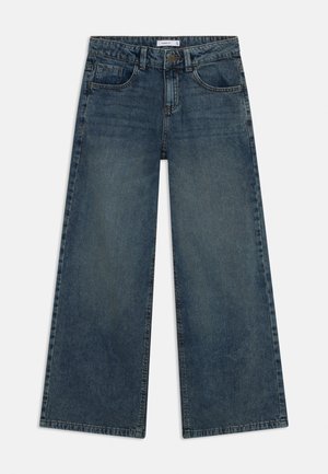 Plati kāju džinsi tumši zilā krāsā ar klasisku piecu kabatu dizainu, pogas aizdari un kontrastējošas šuvju detaļas.