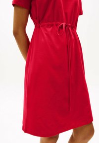 Vestido de algodón rojo con mangas cortas, que presenta un cinturón ajustable en la cintura y una textura suave. El dobladillo es recto y la tela parece ligera.