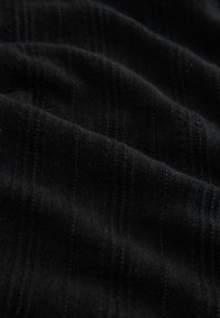 Tela negra con pliegues suaves y una sutil textura de rayas verticales bajo luz tenue.