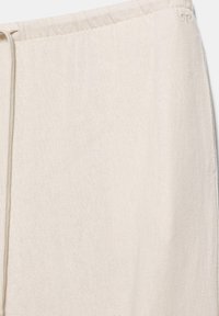 Nahaufnahme von hellbeigen Leinenhosen mit elastischem Bund, Kordelzug und feiner Struktur.