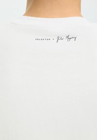 Biała bawełniana koszulka z okrągłym dekoltem bez szwów i nadrukowaną metką na plecach z tekstem "SELECTED x Jules Magistry."