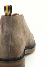 Stivaletto in suede marrone con punta rotonda, dettaglio in pelle a contrasto e linguetta a strisce. Suola in gomma con un design a colori sovrapposti.