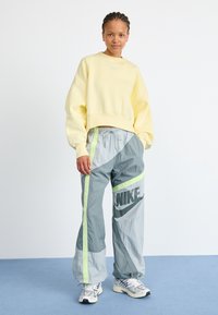 Light yellow cropped sweatshirt with a small logo, paired with gray track pants featuring neon accents and a large logo. Textured, sporty design.