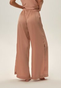 Jasnoróżowe satynowe spodnie o szerokich nogawkach z luźnym krojem, z bocznymi rozcięciami dla swobody ruchów oraz elastycznym pasem dla wygody.