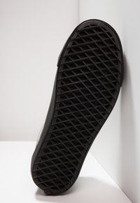 Semelle en caoutchouc noire avec un motif de grille et de losanges, présentée sur un fond blanc en angle.