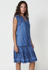 Abito in denim blu con scollo a V e design senza maniche, caratterizzato da dettagli ricamati e una gonna arricciata, che offre una vestibilità comoda.