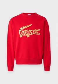 Sudadera roja con un gran diseño gráfico dorado, cuello redondo, puños y dobladillo acanalados, fabricada con tela de algodón suave.