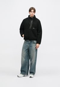 Μαύρο, φλις μισό-φερμουάρ pullover με μπροστινή τσέπη, συνδυασμένο με φαρδιά ρουμπινί τζιν και λευκά αθλητικά παπούτσια.