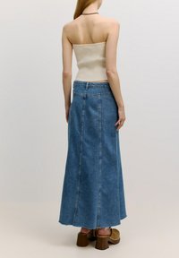 Maxi-Rock aus blauem Denim mit hoher Taille und Nahtdetails, kombiniert mit einem beigen gerippten Tube-Top und braunen Absatzclogs.