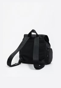 Mochila negra de nailon con correas ajustables, un asa en la parte superior y un bolsillo con cremallera lateral. Diseño compacto con una textura suave y mate.