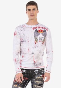 Langarmweißes Hemd mit roten Spritzmustern, einer Grafik mit Flügeln und Krone sowie dem Text "NEW YORK STYLE IN MY HEART". Aus Baumwollmaterial.