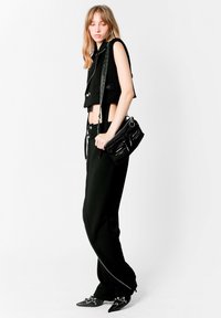 Chaleco negro corto y pantalones de cintura alta, ambos en un material elegante. Los accesorios incluyen un bolso negro pequeño con detalles de cremallera y tacones puntiagudos negros.