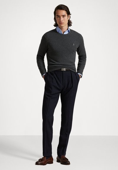 Pulover gri peste o cămașă albă-bleu, asortat cu pantaloni navy cu dungi și mocasini din piele maro. Cureaua simplă cu cataramă metalică.