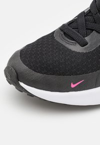 Schwarzer Sportschuh mit einem Mesh-Obermaterial, ausgestattet mit einem pinken Nike-Logo, weißer Zwischensohle und strukturiertem Gummi-Mittelsohle. Die Schnürsenkel sind schwarz.