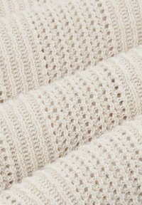 Tessuto lavorato a maglia di colore crema con un motivo texturizzato che alterna punti aperti e chiusi, creando un aspetto morbido e arioso.