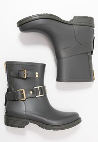 Bottes en caoutchouc grises avec deux accents de boucles dorées. Le design à hauteur de cheville présente une semelle texturée et une finition lisse. Fermeture éclair sur le côté incluse.