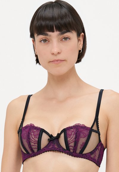 Lacy bra featuring a dark purple floral lace overlay, black mesh panels, and a black satin bow at the center. Adjustable straps included.