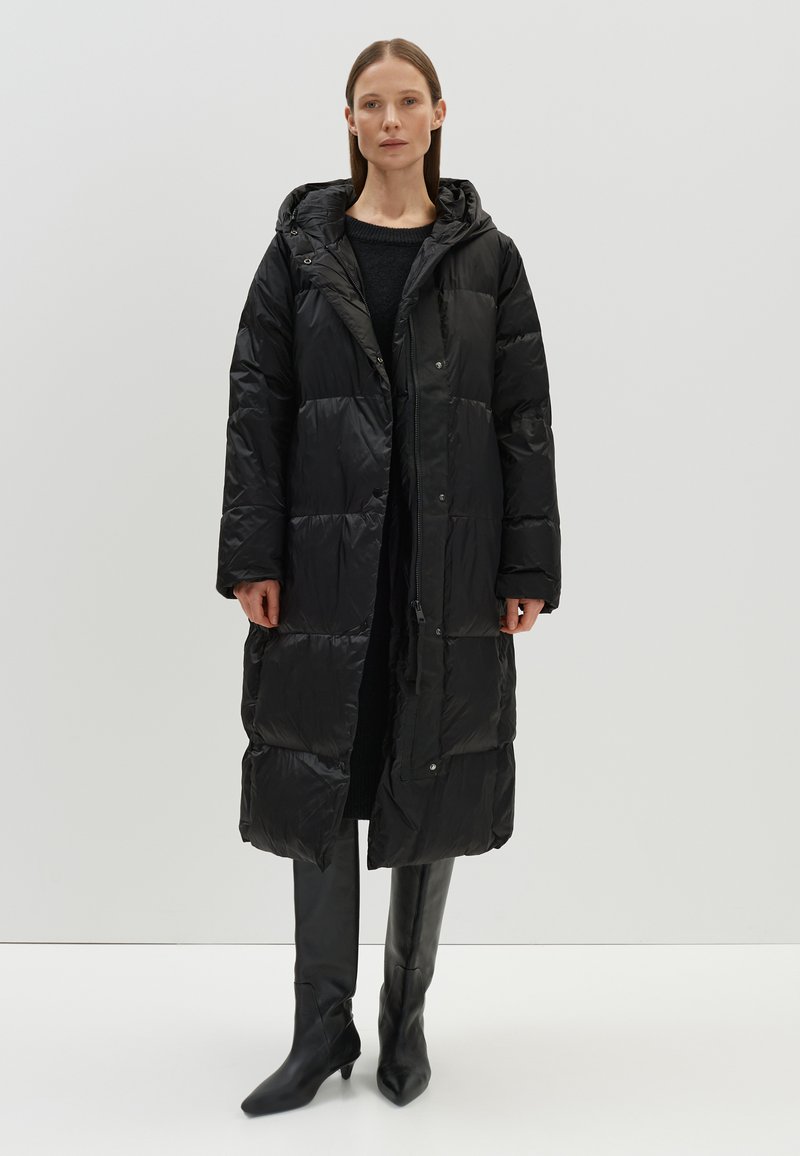 Zwarte pufferjas met capuchon, voorzien van een gestikte motief, ritssluiting en zakken. Gepaard met strakke zwarte hoge hakken.