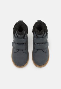 Des bottines en cuir bleu foncé présentent deux sangles Velcro réglables, une doublure en fausse fourrure noire douce et une semelle en caoutchouc marron texturée.