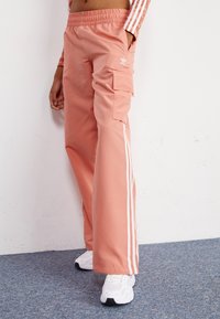 Persikka väriset cargo-housut rentona istuvuutena, joissa on elastinen vyötärö, sivutaskut ja valkoiset raidat sivuilla. Yhdistettynä valkoisiin tennareihin.