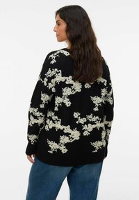 Zwarte trui met crèmekleurige bloemenborduursels, losse pasvorm, lange mouwen en een ronde halslijn, gecombineerd met blauwe denim jeans.