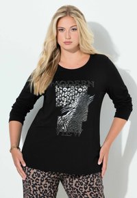 Czarny top z długim rękawem z grafiką i metalicznymi akcentami w srebrze, zestawiony z brązowymi spodniami w panterkę. Miękka tekstura materiału.