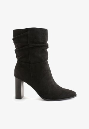 Black suede mid-calf women's boot with slouchy upper, pointed toe, and block high heel on a white background.